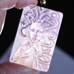 Purple agate Medusa pendant held against light to show the carved face and snakes