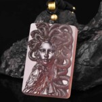Purple agate Medusa necklace with a carved face and coiled snakes on a dark rock
