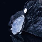 Raw aquamarine necklace with pale blue stone, black cord and silver-tone surround